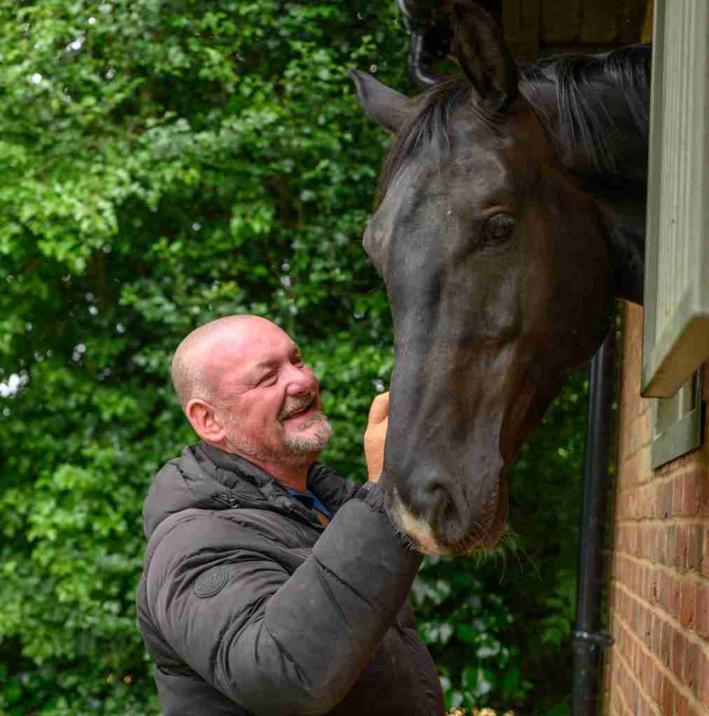 A man greeting a dark bay horse at the stable door